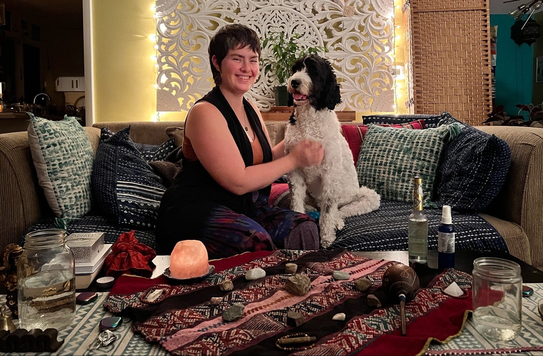 Mackenzie sits on a couch with dog Peaches, surrounded by ritual items on a table.