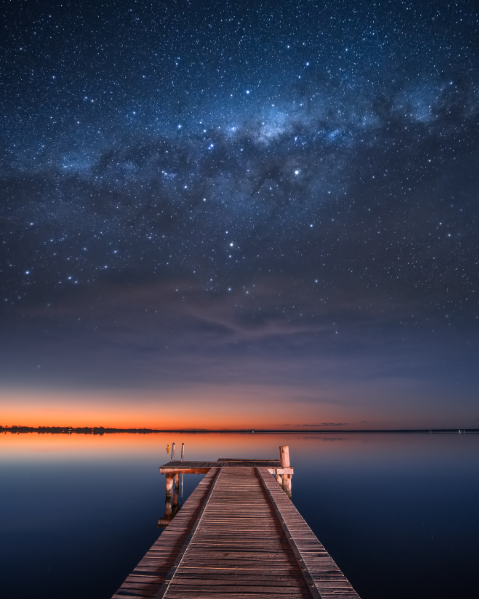 A dock over water at dusk with the cosmos shining in the sky.
