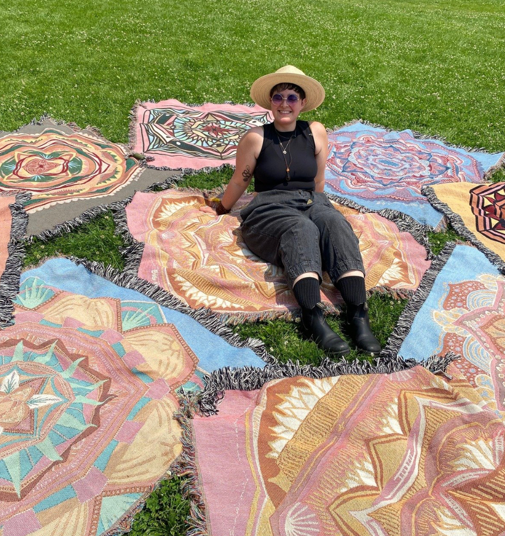 Mackenzie sits amongst colorful woven ritual blankets laid on the grass.